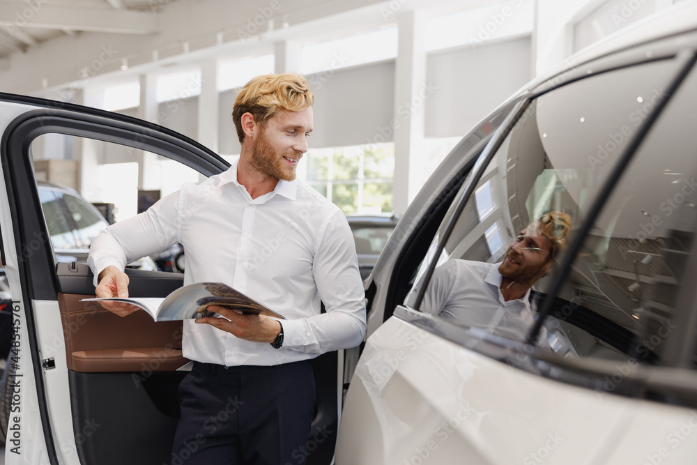 Man serious customer male buyer client wear white shirt read car papers documents agreement choose auto want buy new automobile in showroom vehicle dealership store motor show indoor Sales concept