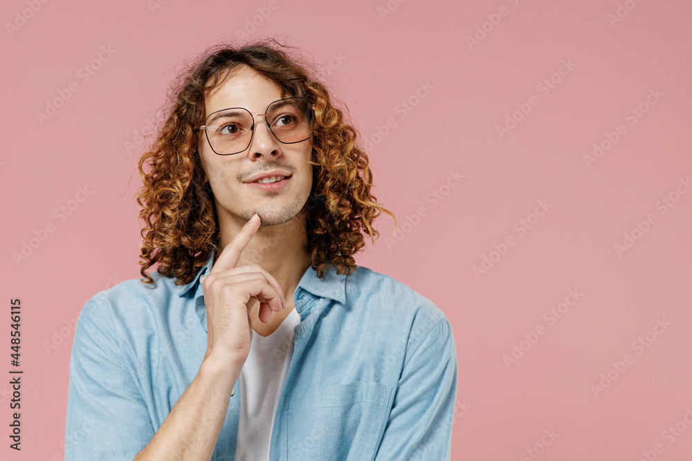 Young minded happy man 20s with long curly hair wear blue shirt white t-shirt glasses prop up chin look aside isolated on pastel plain pink color background studio portrait. People lifestyle concept