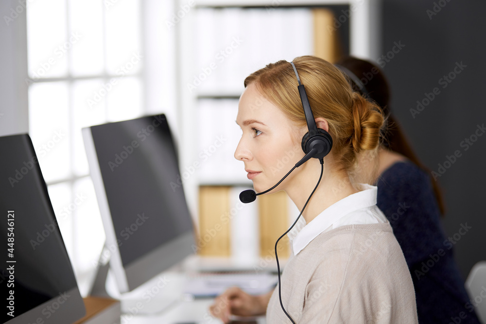 Friendly businesswoman talking by headset while sitting in office. Call center and diverse people group in business Friendly businesswoman talking by headset while sitting in office. Call center and diverse people group in business