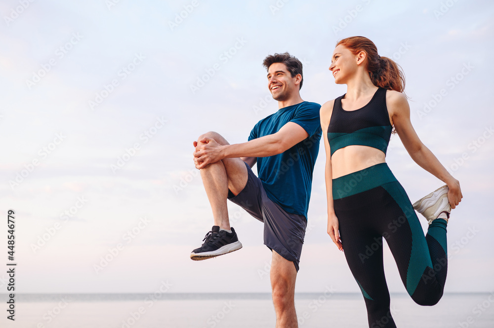 Lower couple young two friend strong sporty sportswoman sportsman woman man in sport clothes warm up training do stretch exercise on sand sea ocean beach outdoor jog on seaside in summer day morning. - obrazy, fototapety, plakaty 
