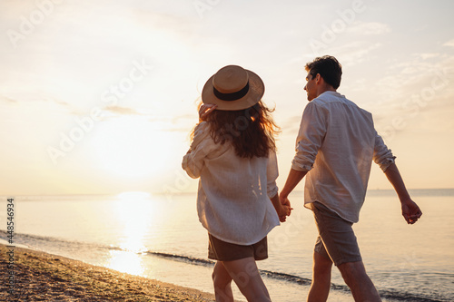 Obraz na plátně Back rear view young happy couple two friends family man woman 20s in white shirt clothes hold hands walk stroll together at sunrise over sea beach ocean outdoor exotic seaside in summer day evening