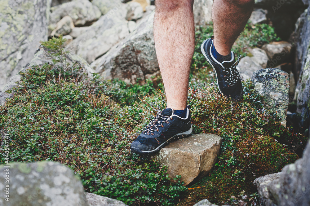 Young hiker crosses stone steps in hiking boots