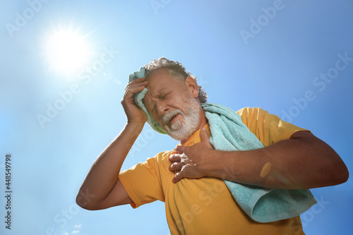 Fototapeta Senior man with towel suffering from heat stroke outdoors, low angle view