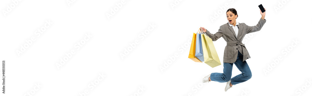 Amazed woman with shopping bags and smartphone jumping isolated on white, banner