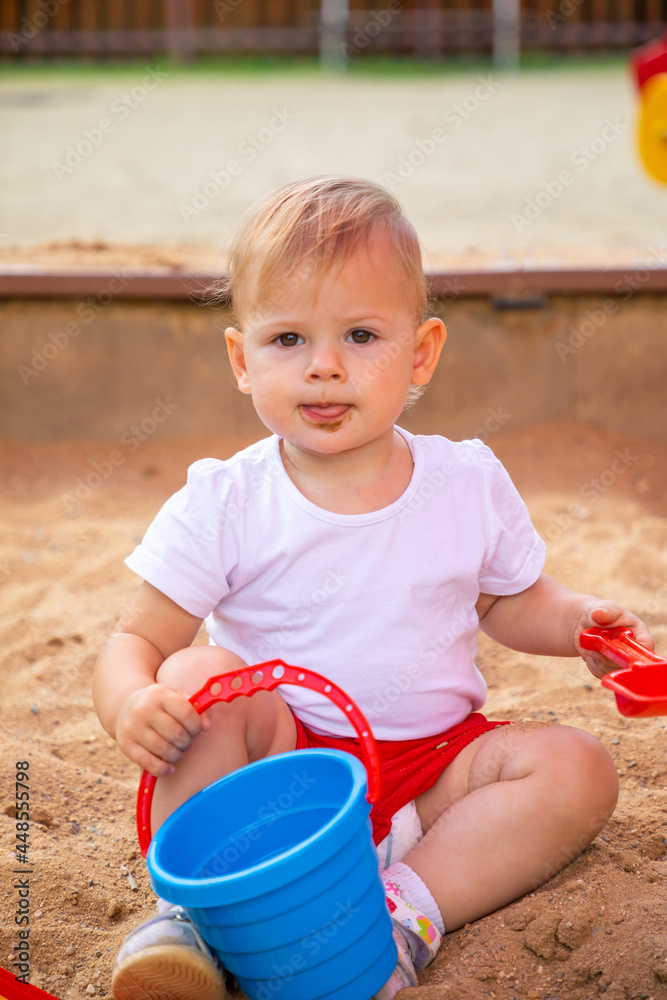 Adorable toddler girl playing with sand on sandbox in playground Adorable toddler girl playing with sand on sandbox in playground