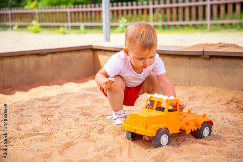 Adorable toddler girl playing with sand on sandbox in playground Adorable toddler girl playing with sand on sandbox in playground
