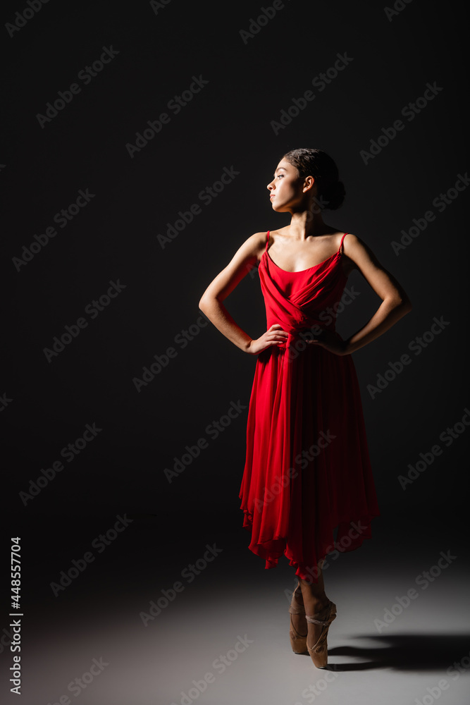Side view of ballerina holding hands on hips in light on black background Side view of ballerina holding hands on hips in light on black background
