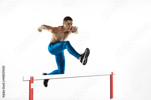 Steeplechase. Young male athlete, runner running, jumping isolated on white studio background. Muscular, sportive man. Concept of sport, healthy lifestyle