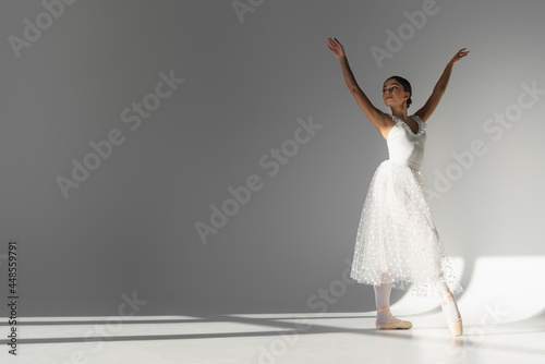 Young ballerina in white dress dancing on grey background