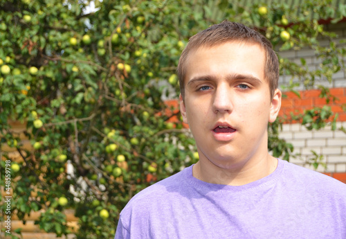 Autistic behavioral traits.A young autistic guy stands with his mouth open on the street near the house photo