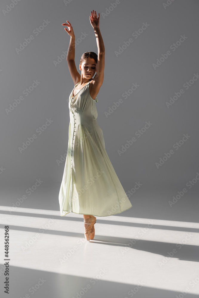 Fototapeta premium Pretty ballerina in dress spinning on grey background with sunlight