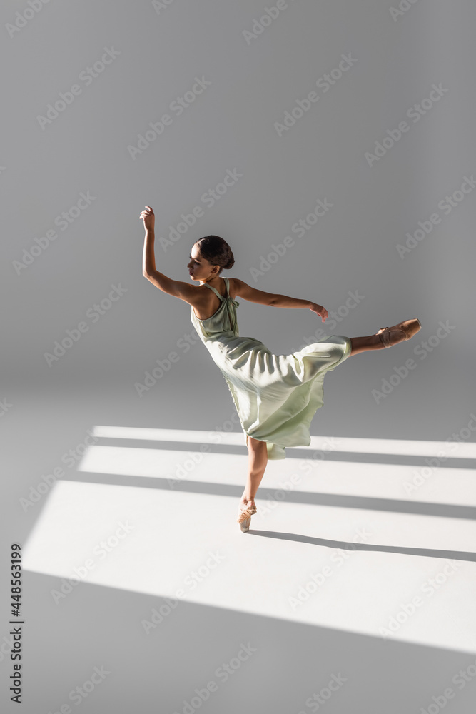 Ballerina dancing and standing on one leg on grey background with sunlight