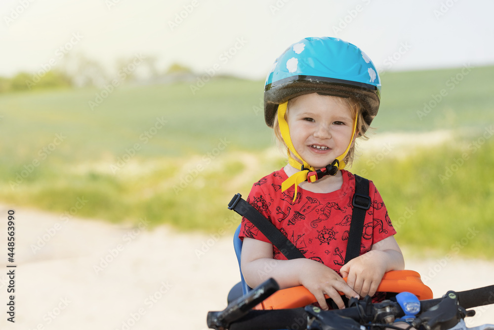 Smiling little boy with safety helmet on the head is posing in bicycle seat. All potential trademarks are removed. Smiling little boy with safety helmet on the head is posing in bicycle seat. All potential trademarks are removed.