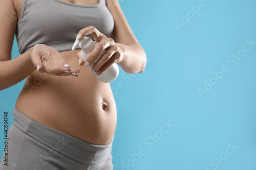 Pregnant woman with cosmetic product on light blue background, closeup. Space for text