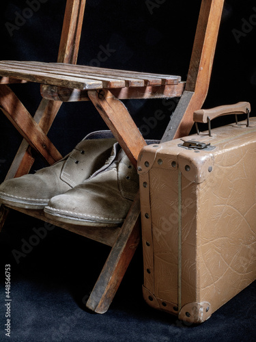 A migrant's suitcase, with a pair of broken shoes, under a small and modest wooden chair.
