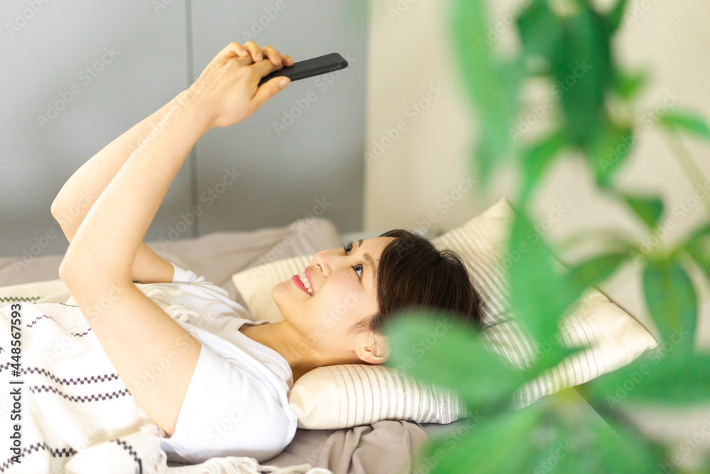 Fototapeta premium ベッドでスマホを使う若い女性