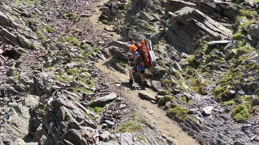 A tourist descends from a cliff along a mountain path, holding on to the rope of the vertical railing. Climbing Kazbek from the north, from Russia. Hike across the Caucasus. A tourist descends from a cliff along a mountain path, holding on to the rope of the vertical railing. Climbing Kazbek from the north, from Russia. Hike across the Caucasus.