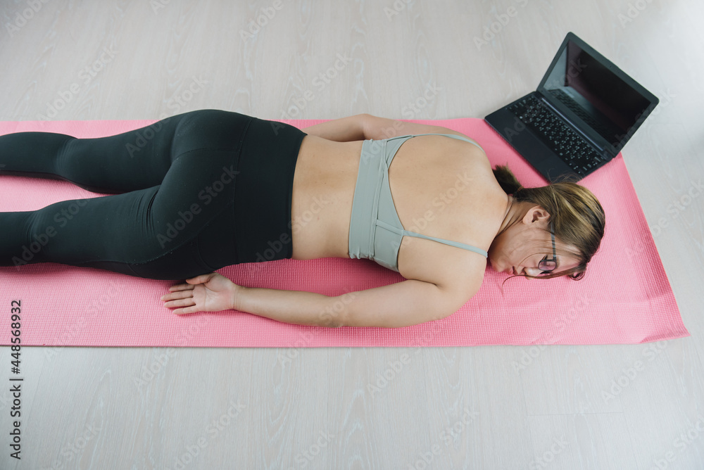 Naklejka premium Tired after exercise and workout. Overtraining concept. Exhausted young asian woman lying on floor and resting after heavy online training in home gym at yoga mat.
