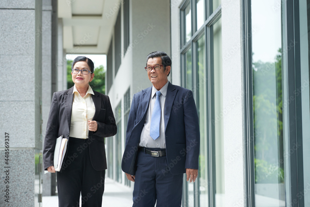 Smiling senior businessman and businesswoman walking along the street of city downtown