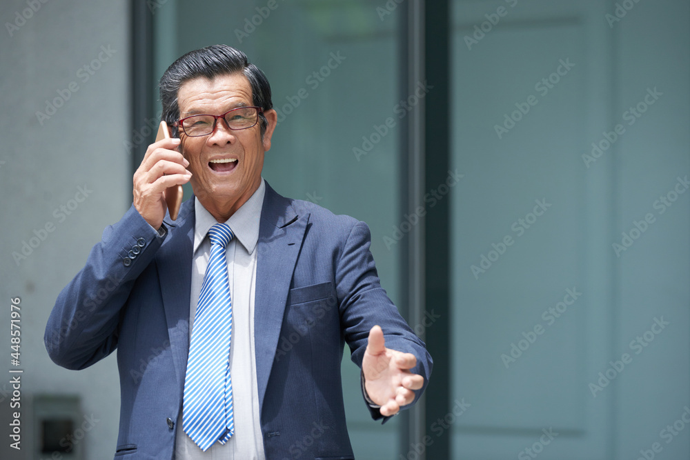 Excited aged businessman standing outside the office building and talking on phone with customer Excited aged businessman standing outside the office building and talking on phone with customer