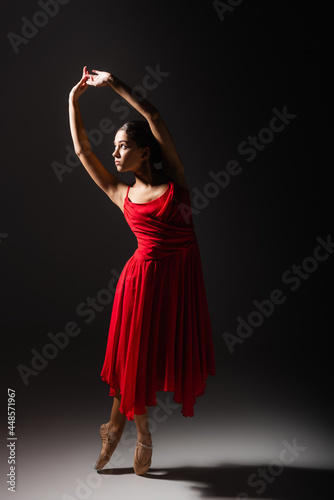 Side view of woman in pointe shoes dancing on black background with light