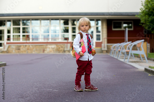 Preschool blond child, cute boy in uniform, hodling apple and book, going in preschool for the first time after summer