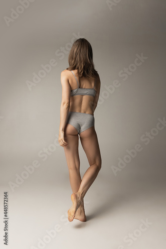 Portrait of young beautiful slim woman in lingerie posing isolated over gray studio background. Natural beauty concept. Back view