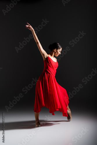 Side view of young ballerina dancing on black background