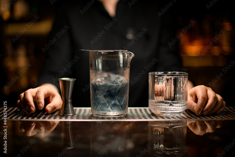 Close-up of mixing cup with cold cocktail and old-fashioned glass and jigger on the bar