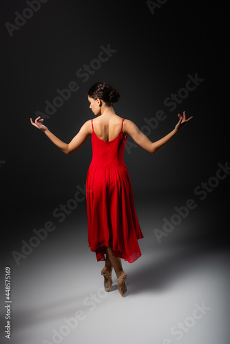 Side view of ballerina in red dress looking away on black background