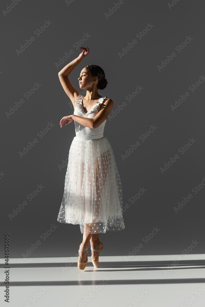 Side view of young ballerina with closed eyes dancing on grey background with sunlight Side view of young ballerina with closed eyes dancing on grey background with sunlight