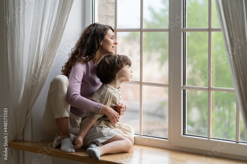 Slika na platnu Curious mom and kid boy looking outside sitting on window sill