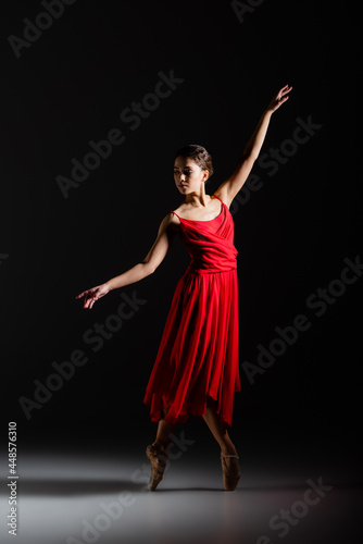 Ballerina in red dress dancing on black background