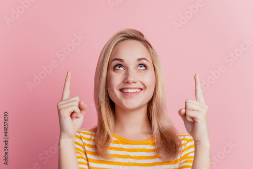 Portrait of dreamy promoter girl indicate fingers up look empty space toothy smile on pink background