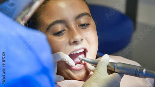 Young caucasian female with dentist in white latex gloves check condition of her teeth. baby girl in blue dental chair.