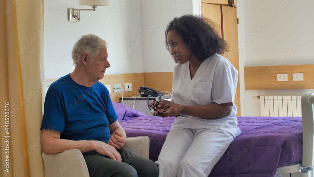 African female doctor visiting elderly male patient in hospital bed. Rehabilitation and retirement concept African female doctor visiting elderly male patient in hospital bed. Rehabilitation and retirement concept
