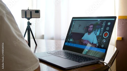 a young man takes pictures of himself on the phone and displays the video on the laptop screen