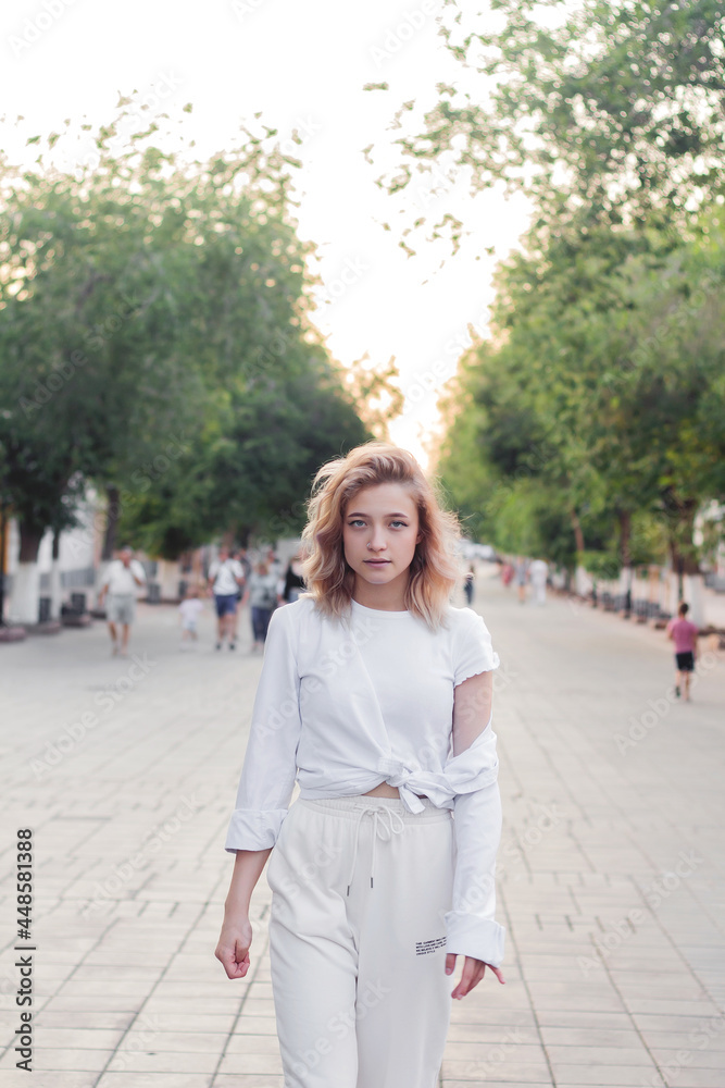 Portrait of a beautiful young woman in white clothes on the alley of the city