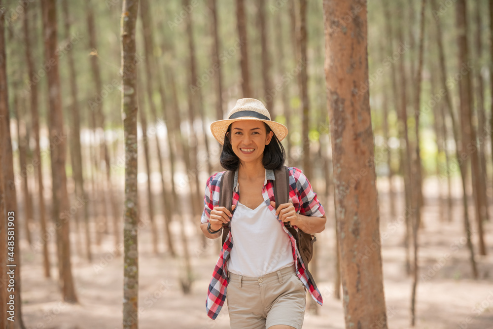 people and lifestyles adventure, travel, tourism, hike and people concept - traveller women walking in the forest of smiling  walking with backpack, hat in woods.
