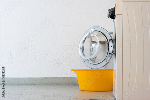 Landry room washing machine open door and yellow plastic basket. Side view no people photo