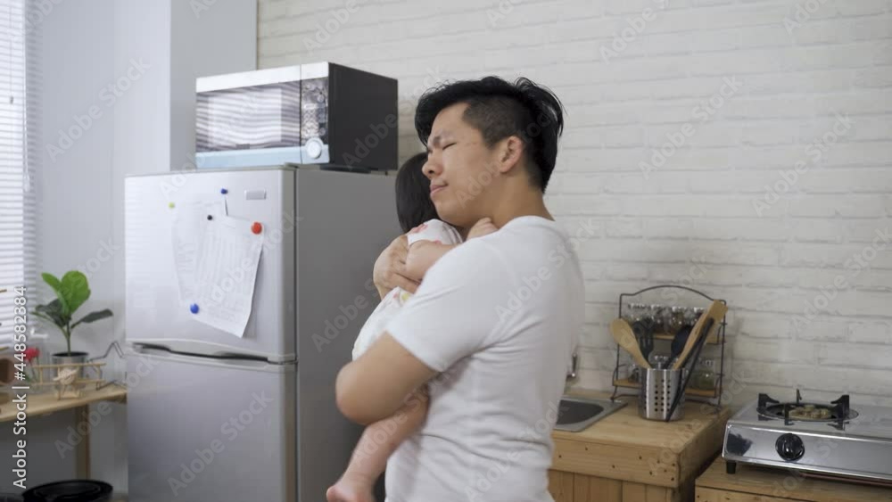 young asian new father is hugging and lulling his toddler child to sleep with eyes closed and gentle rock in the kitchen at home. young asian new father is hugging and lulling his toddler child to sleep with eyes closed and gentle rock in the kitchen at home.