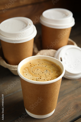 Obraz na płótnie Takeaway paper coffee cups with plastic lids and cardboard holder on wooden tabl