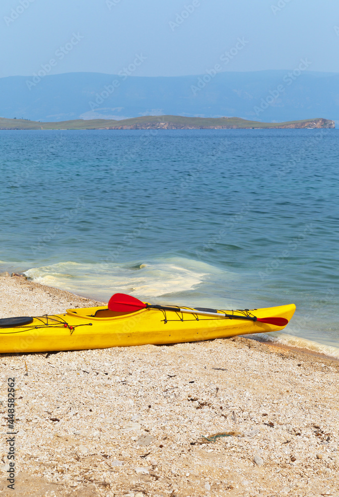 Yellow tourist kayak on the shore of Baikal Lake on a summer sunny day before traveling by water. View from the coast of Olkhon Island to the Small Sea. Summer outdoor activities concept Yellow tourist kayak on the shore of Baikal Lake on a summer sunny day before traveling by water. View from the coast of Olkhon Island to the Small Sea. Summer outdoor activities concept