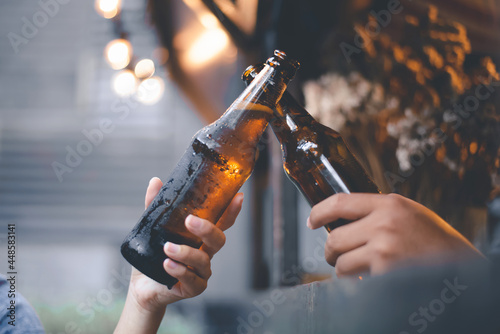 Cropped image of friends having fun clinking bottles of beer while resting at the pub