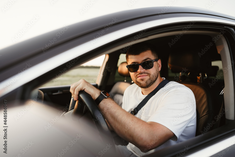 Bearded man driver in sunglasses sitting in his car and looking at camera Bearded man driver in sunglasses sitting in his car and looking at camera