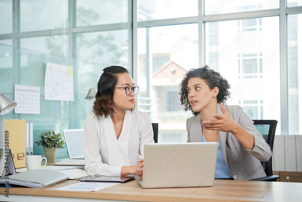 Female entrepreneurs having brainstorming session after watching product presentation on laptop screen at meeting Female entrepreneurs having brainstorming session after watching product presentation on laptop screen at meeting