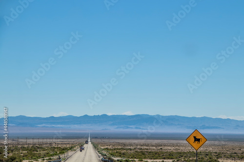 Sign indicating watch out for bulls on desolate Nevada two land road through scub with mountains in background and trucks and a motorcycle approaching