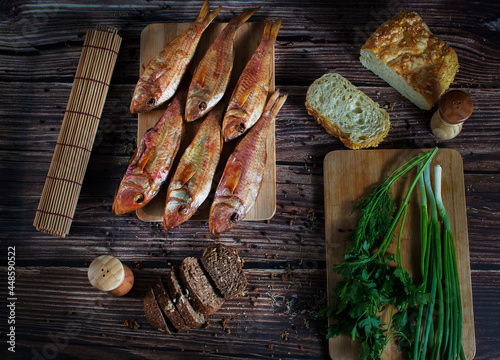 Red mullet fish is laid out on a tree, next to greens, black and white bread. Horizontal orientation.