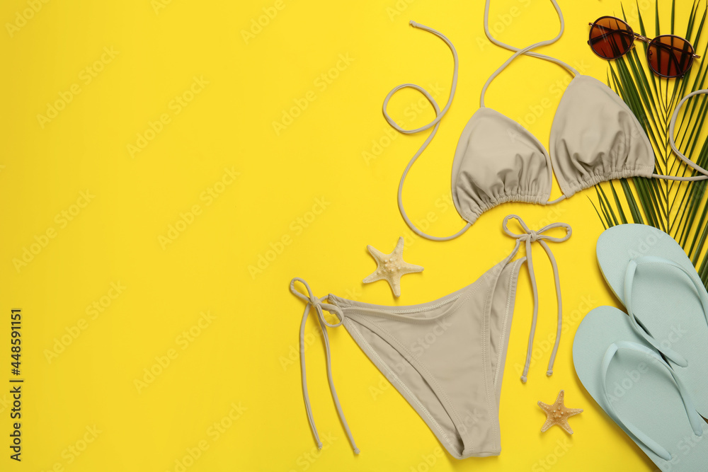 Stylish beige bikini and beach accessories on yellow background, flat lay. Space for text