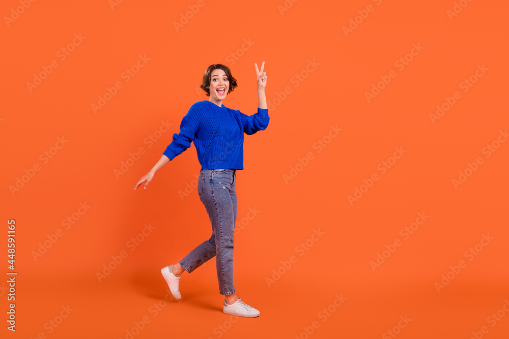 Full length body size view of attractive cheerful girl walking showing v-sign isolated over bright orange color background Full length body size view of attractive cheerful girl walking showing v-sign isolated over bright orange color background